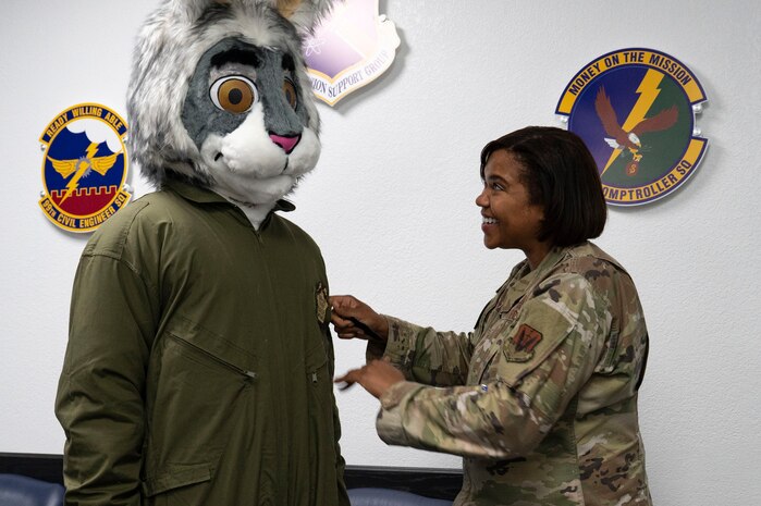 U.S. Air Force Chief Master Sgt. Adrienne Warren, 99th Air Base Wing (ABW) command chief, puts a 99th ABW patch on BUCKET$, the Las Vegas Aces mascot, at Nellis Air Force Base, Nevada, June 9, 2023.