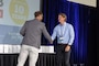 Two men are on a stage shaking hands as an award is presented.