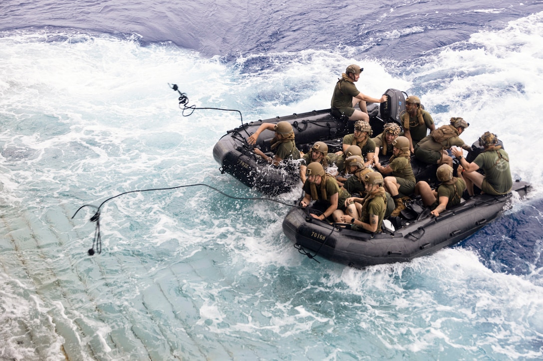 Marines riding in two small boats throw anchors onto a ship's deck.