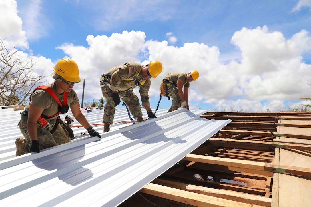 Three soldiers wearing protective gear repair a roof.