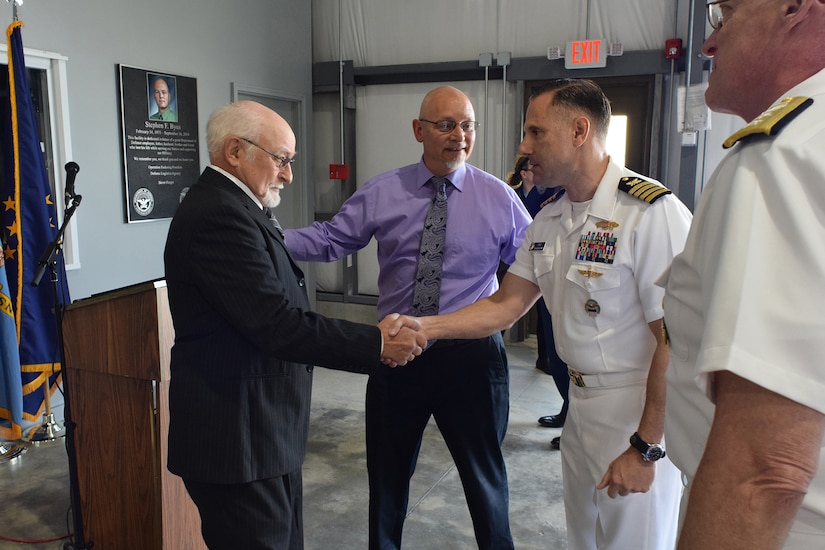 A uniformed service member shakes hands with a man while others look on.