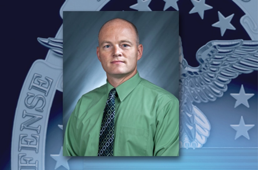 Headshot photo of man in green shirt and blue-patterned tie.