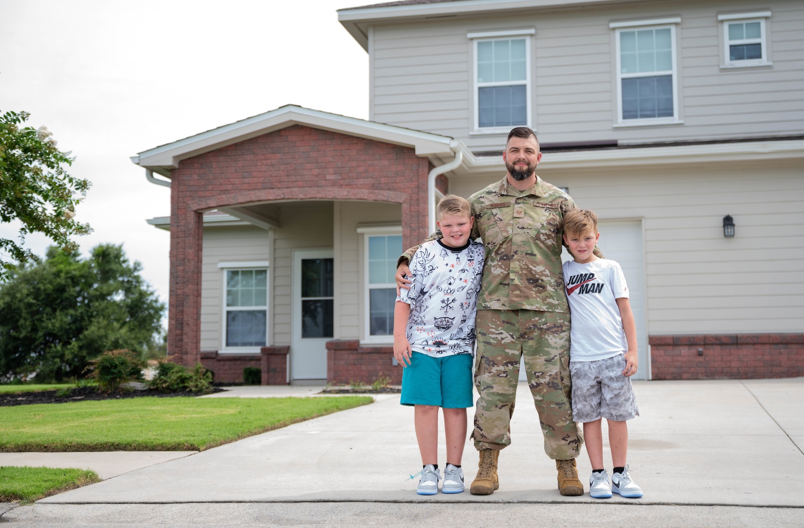 A serviceman and two young boys stand in front of a house