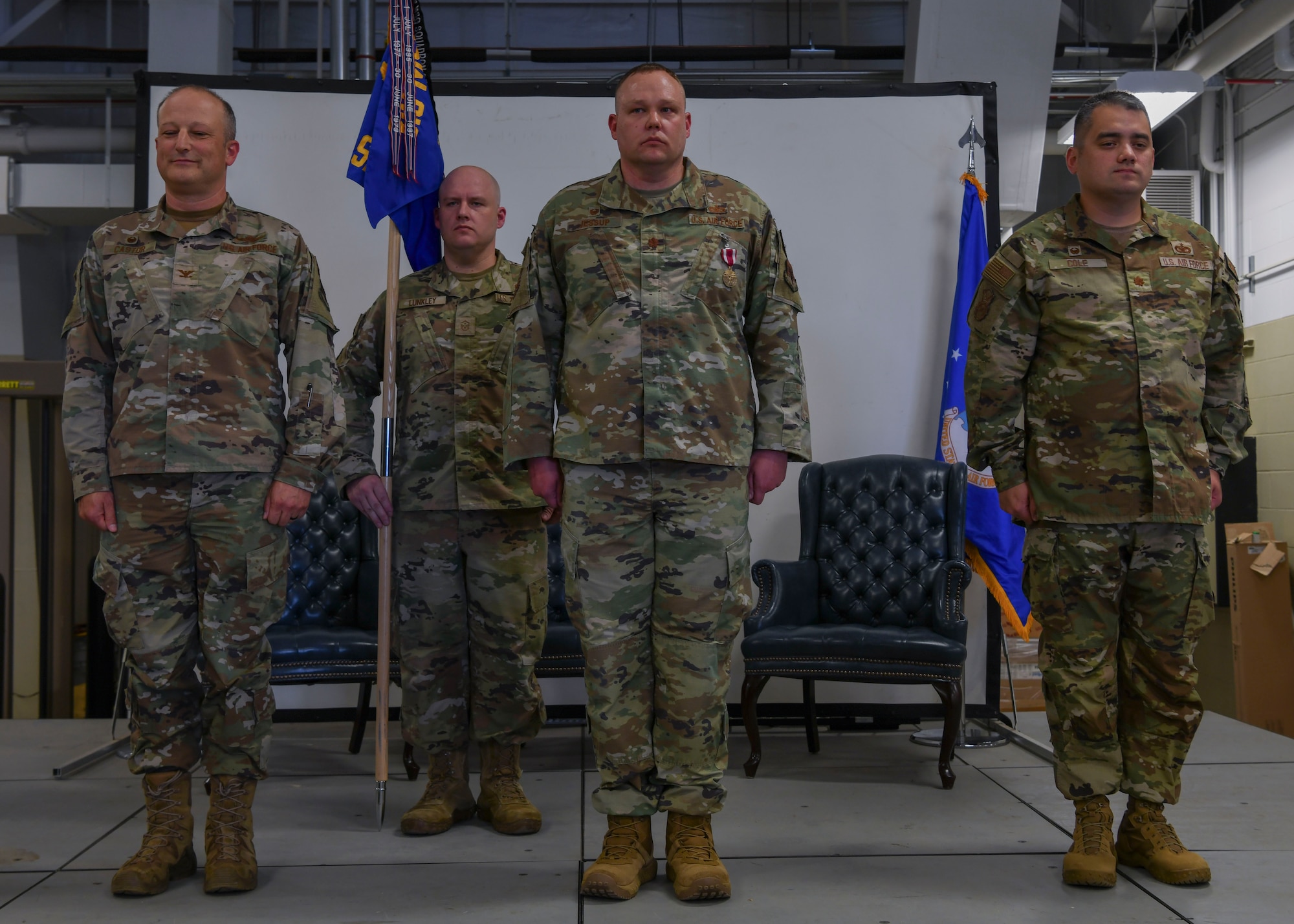 Four men in green uniforms stand at attention.