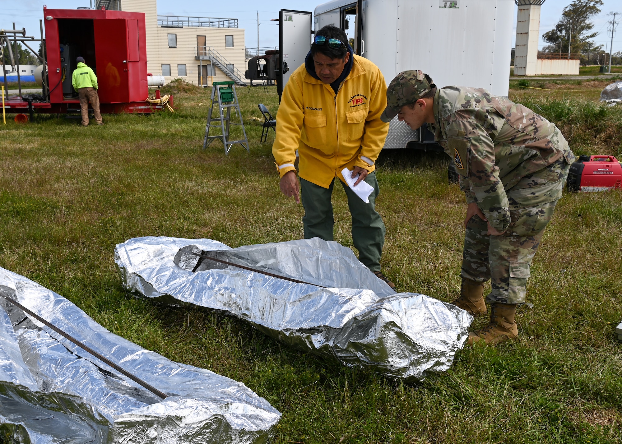 Ralph Gonzales, U.S. Forest Service National Technology and Development Program fire and aviation program manager, explains details about a fire shelter to U.S. Air Force Staff Sgt. Joseph Avenida, 30th Civil Engineer Squadron, at Vandenberg Space Force Base, Calif., May 11, 2023. The fire shelter is a fire-resistant tent-like product that all wildland firefighters carry while on duty. In circumstances when they cannot escape advancing flames, firefighters are trained to ditch their gear, pull out their fire shelter, and climb inside as the flame front passes. Firefighters from the base and the U.S. Forest Service conducted test burns on Vandenberg to simulate real-world fire conditions, helping the firefighters enhance their training. (U.S. Space Force photo by Senior Airman Tiarra Sibley)