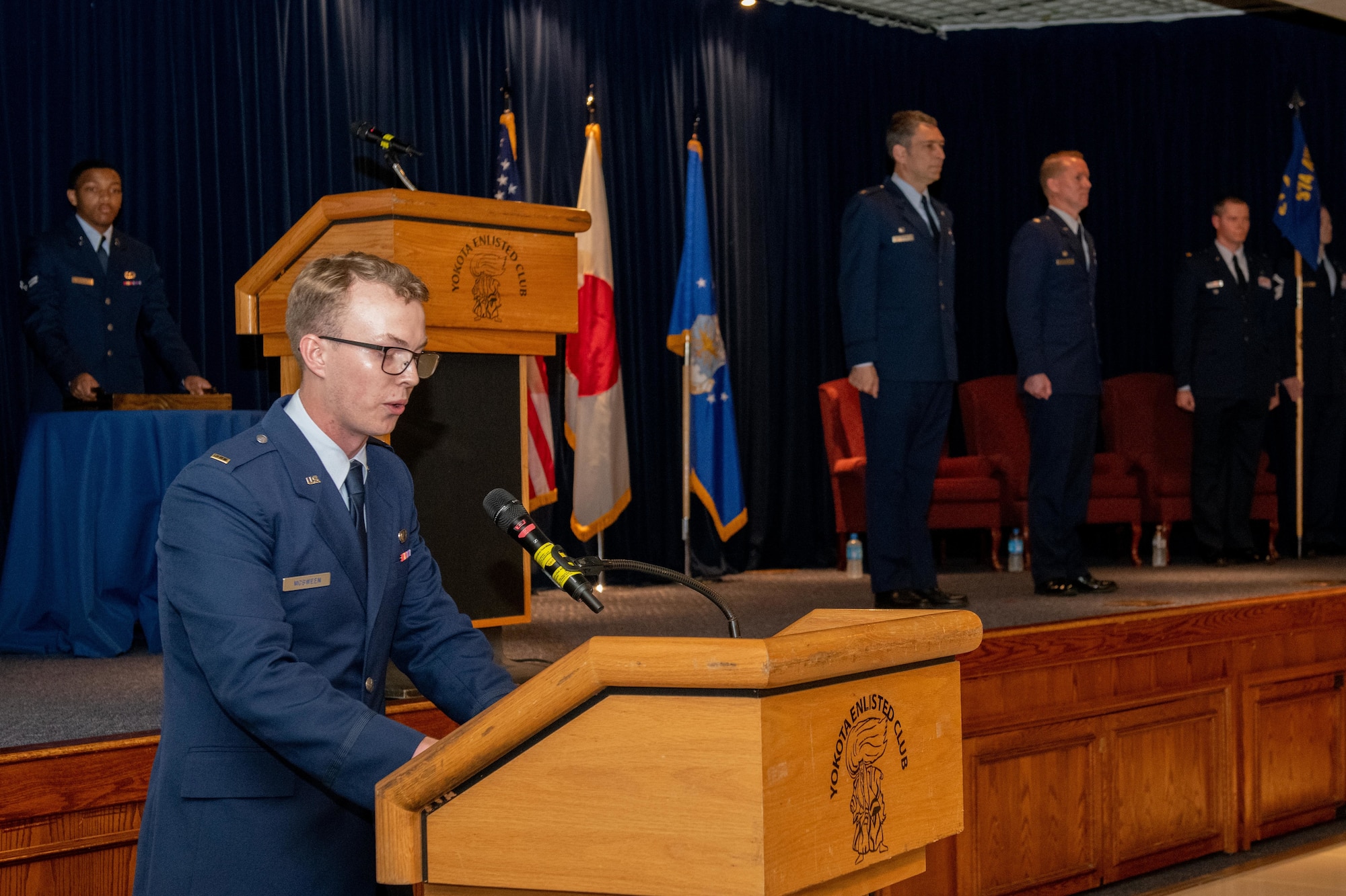 2nd Lt. Andrew Mcsween speaks at the podium and the official party stand on stage.