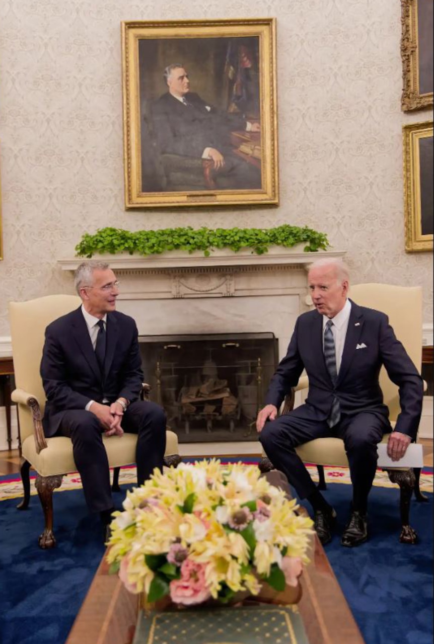 Two men dressed in business suits sit in a room and talk.