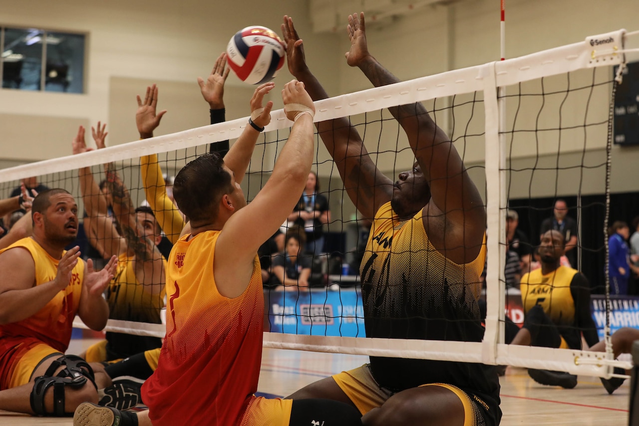 Seated volleyball players faceoff at the net.