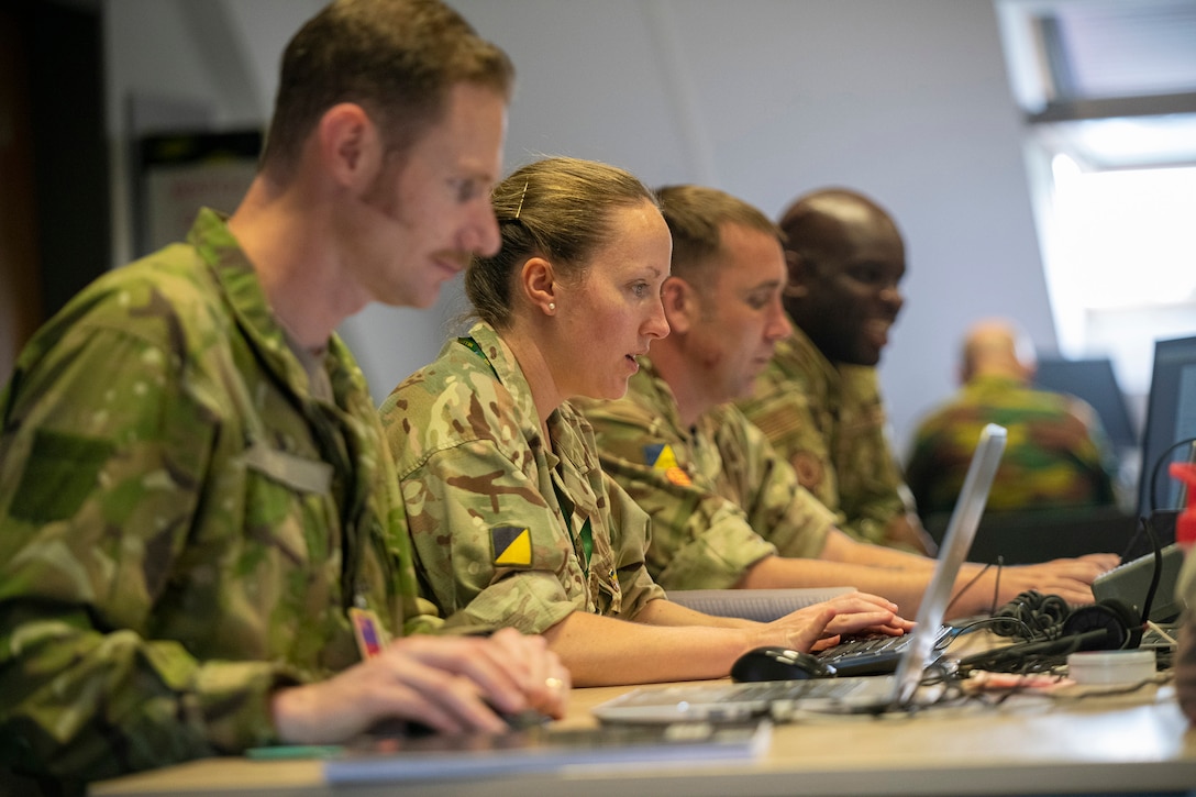 U.S. and U.K. service members work on laptops at a table.