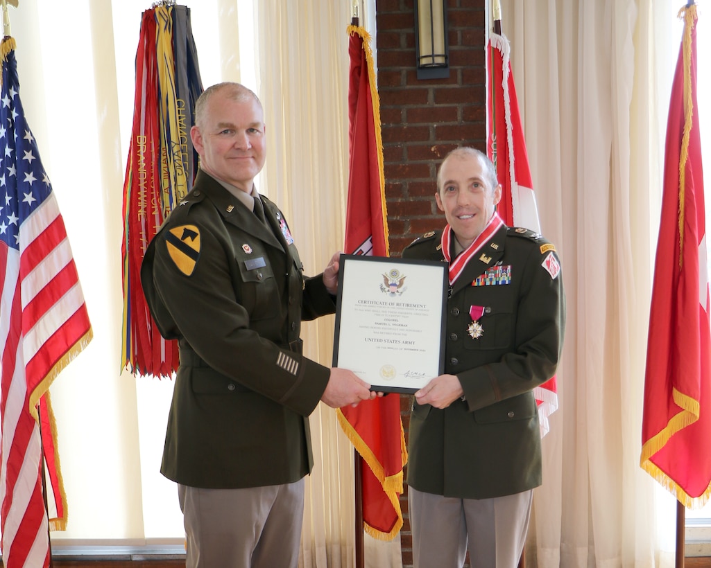 Two men stand in Army uniforms. One hands the other a certificate.