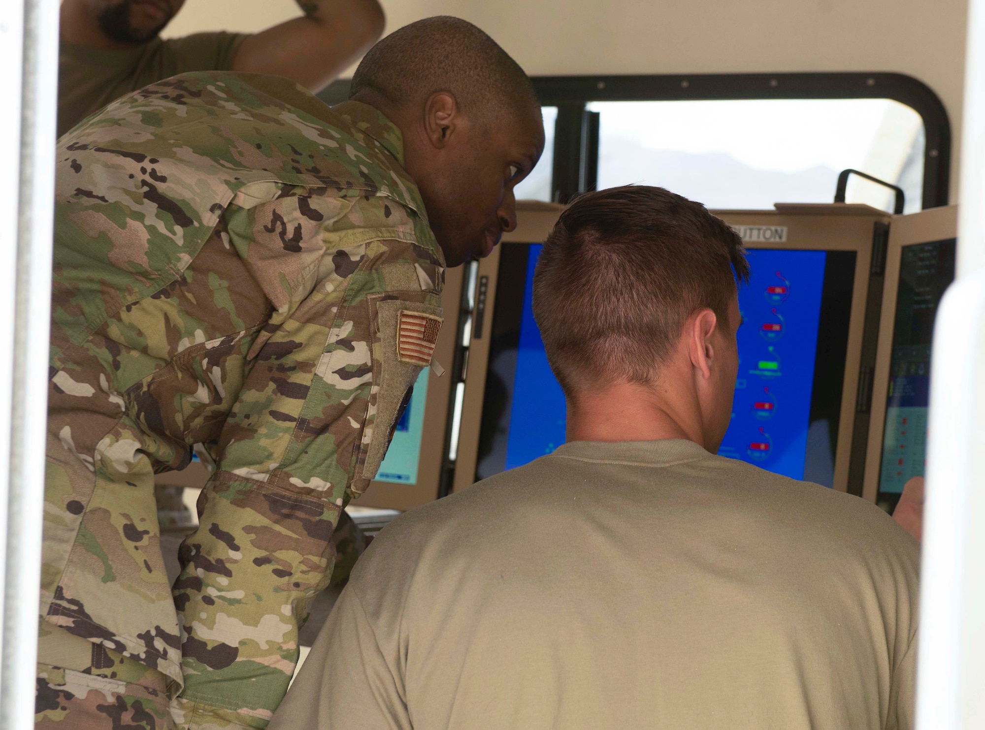 A man in a military uniform looks at a screen next to a man in a green shirt.