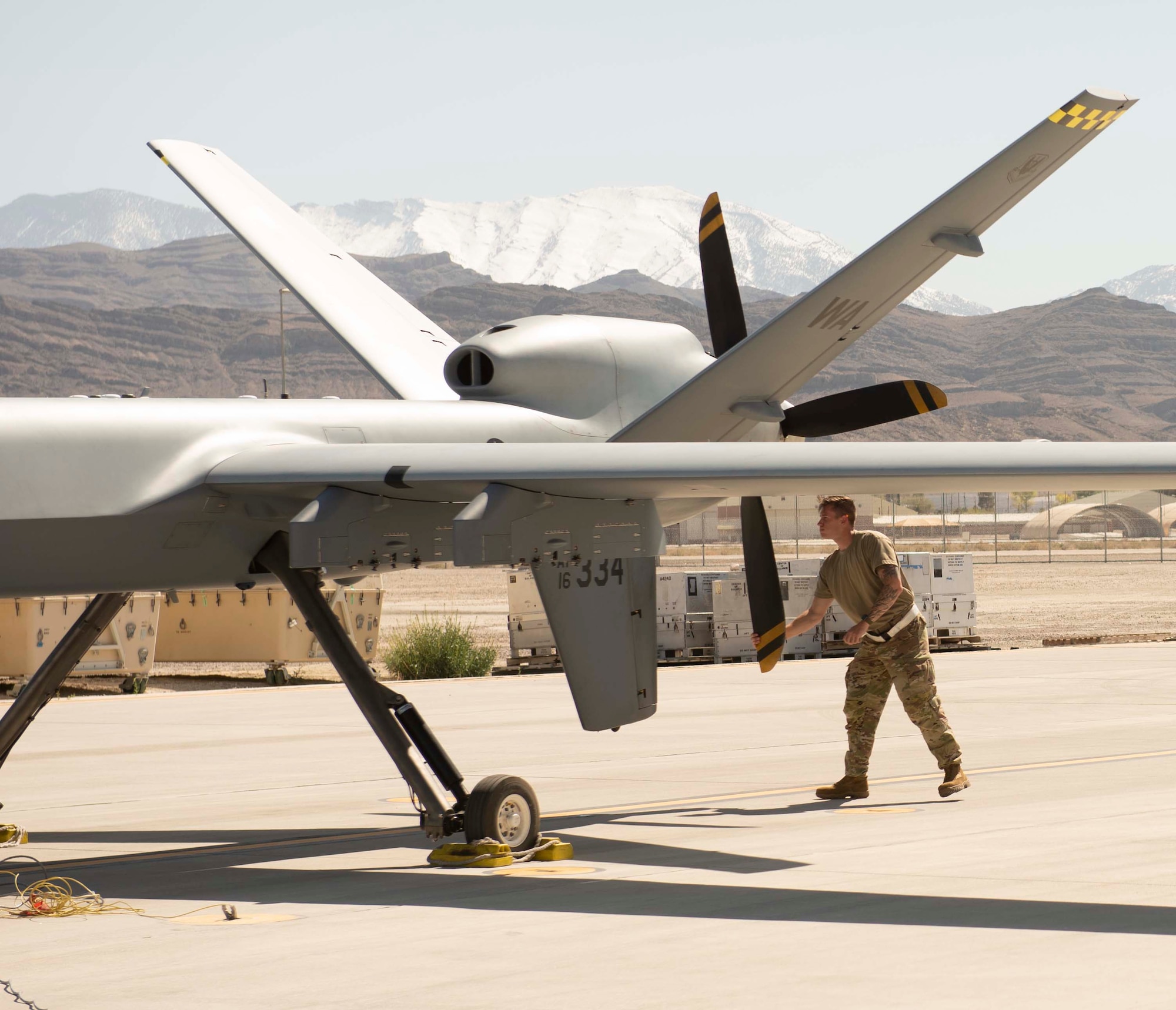 A man in a military uniform checks the propeller of an unmanned aircraft.