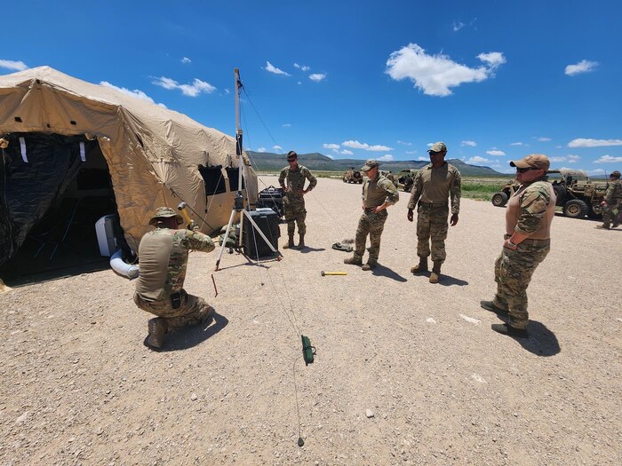 Airman stand around an antenna by a tent in a remote area