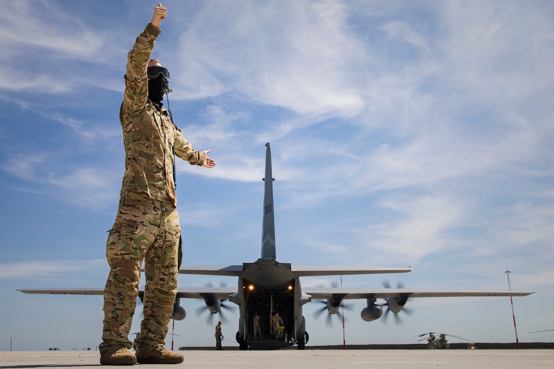 An airman directs military personnel onto a C-130.