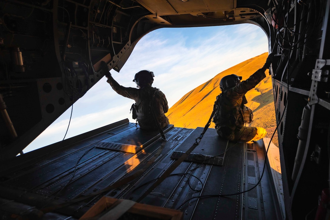 Two guardsmen sit on the ramp of an airborne helicopter.