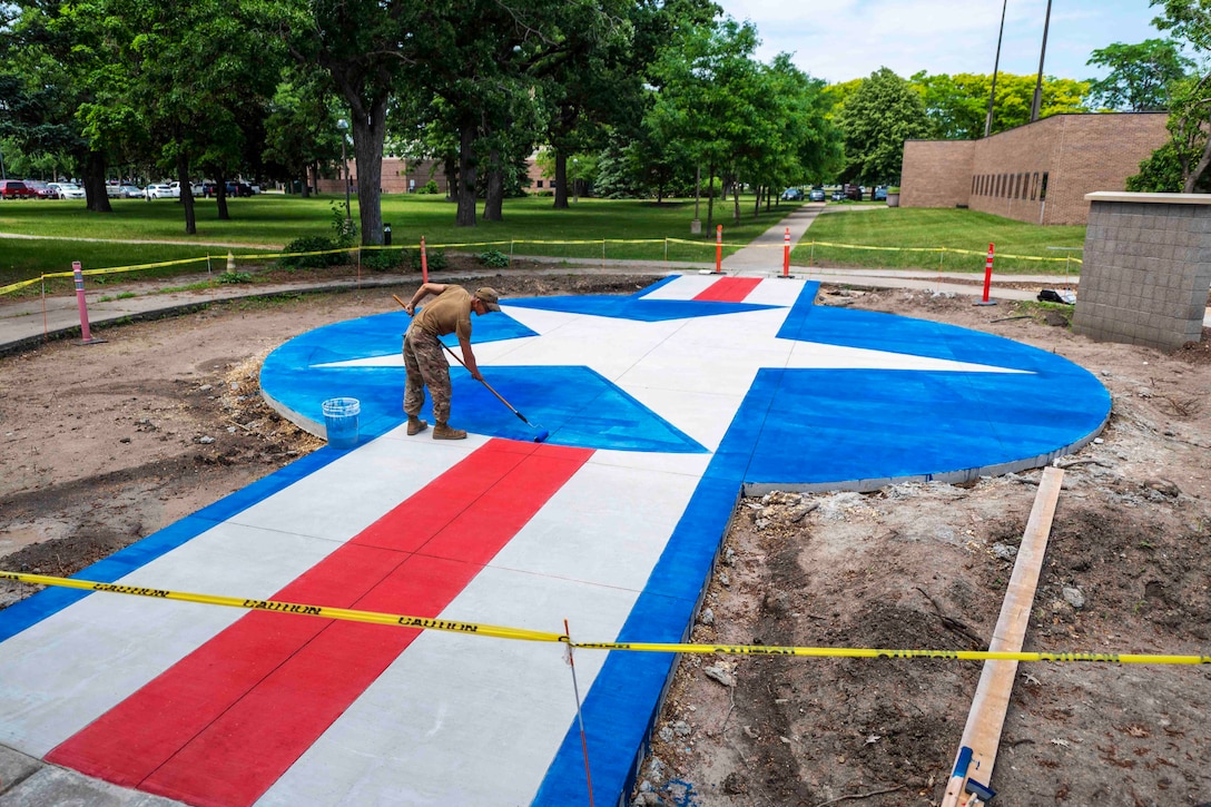 An airman paints a concrete pad with a red, white and blue stripe and star design.