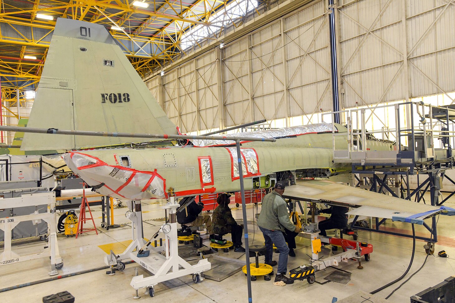 Artisans assigned to Fleet Readiness Center Southeast’s F-5 Production Line prepare to remove the wing of an F-5N Tiger II for inspection