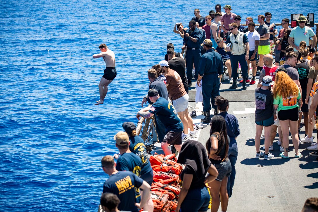 A sailor jumps off the deck of a ship into a body of water as fellow sailors watch.