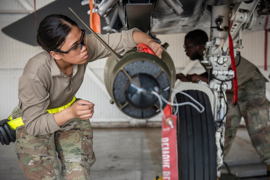 Two airmen secure an unarmed munition to a fighter jet.