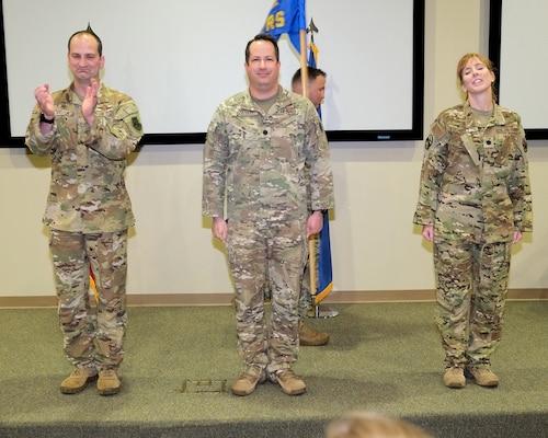 four uniformed military members stand on stage during change of command ceremony.