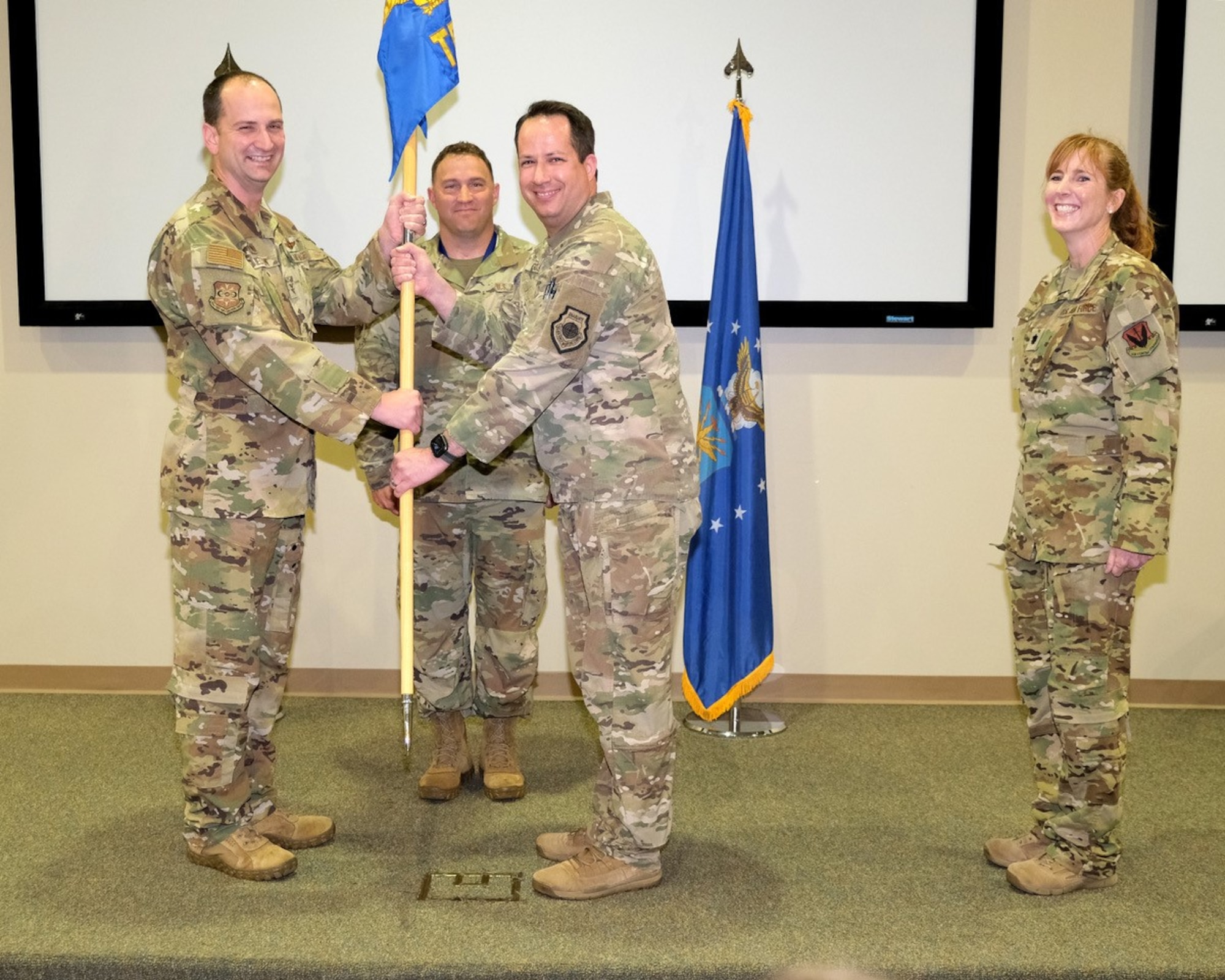 four uniformed military members stand on stage during change of command ceremony.