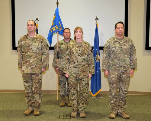 four uniformed military members stand on stand during change of command ceremony.