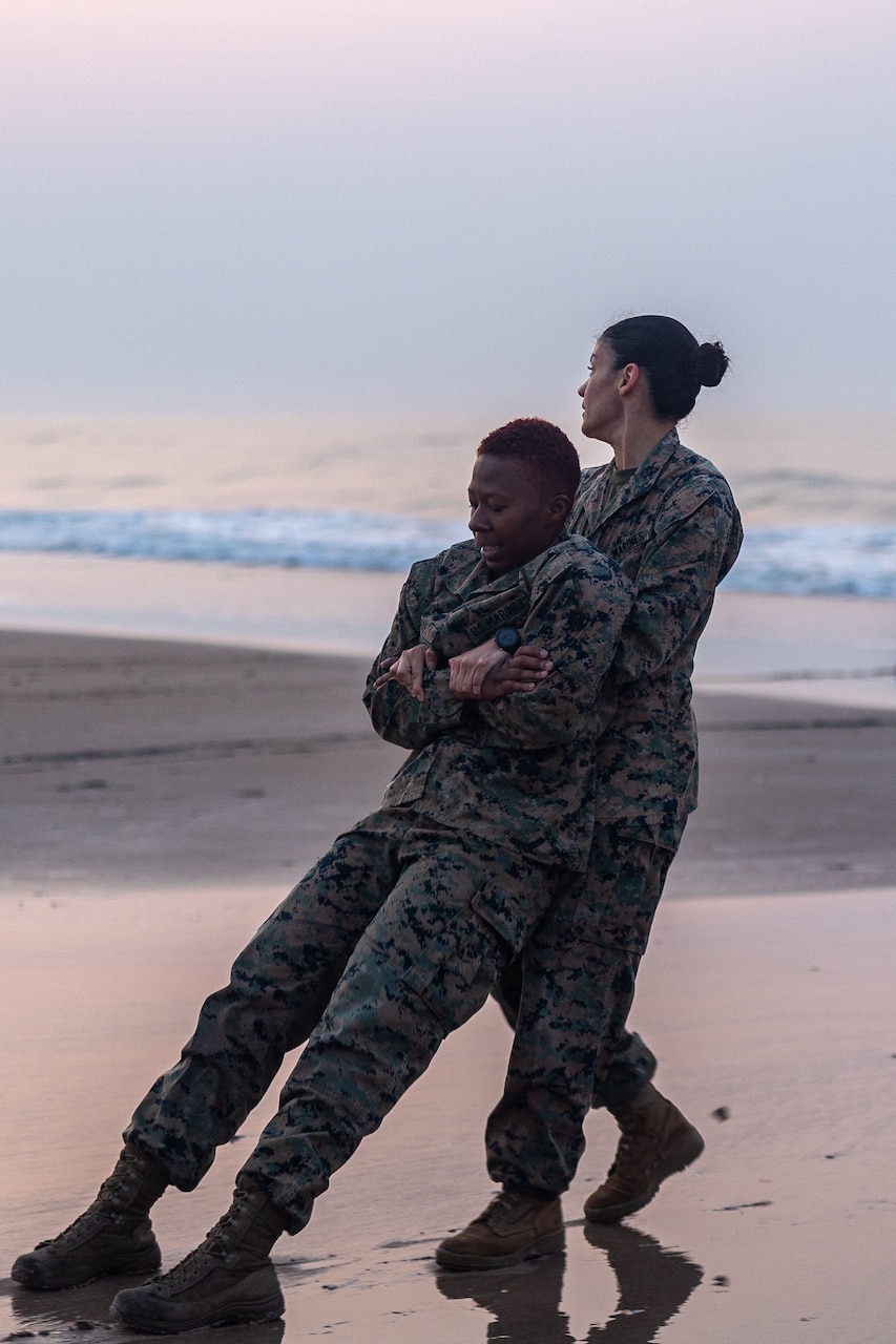 A Marine drags a fellow Marine on the beach during training.