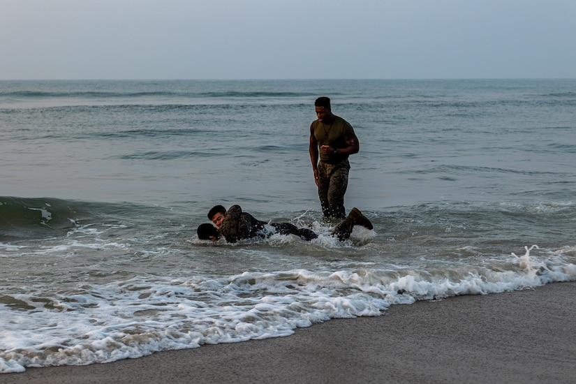 Marines grapple in the beach as a fellow Marine watches.