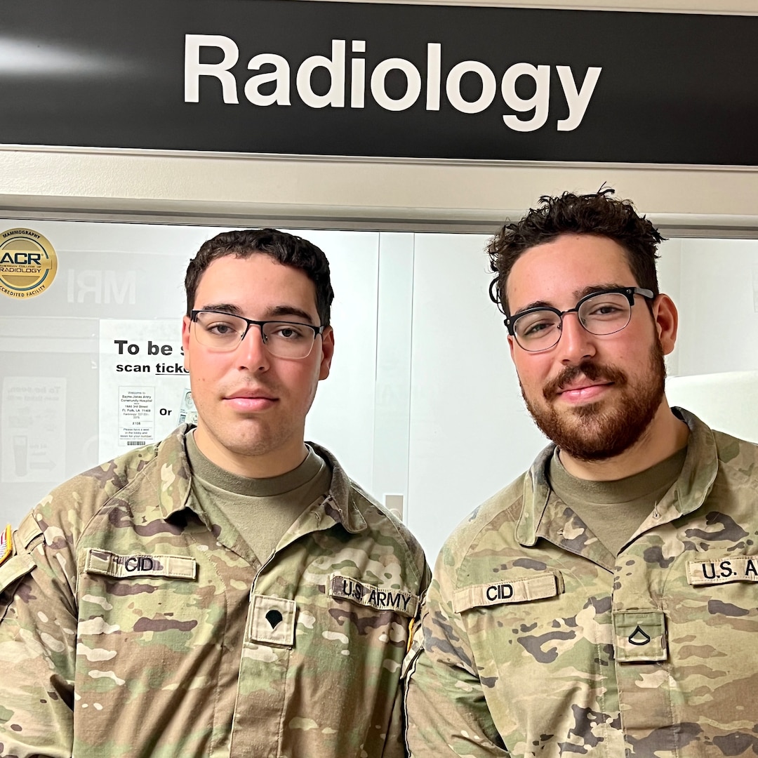 Twin brothers and Soldiers pose in front of a radiology sign at BJACH.