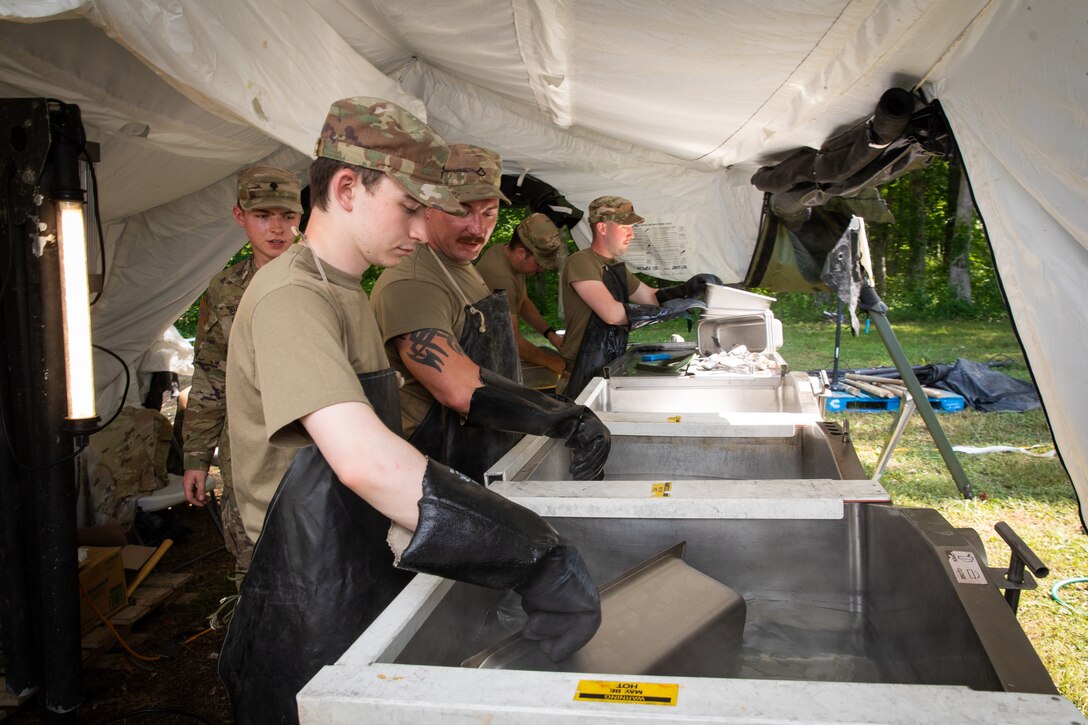 Soldiers of the 1-149th Infantry Battalion, 75th Troop Command, clean cooking equipment in the field sanitation tent during the Regional Philip A. Connelly Field Feeding Competition at the Harlold L. Disney Training Center in Artemus, Kentucky on June 14, 2023. The Soldiers are competing against nine other states and territories National Guard field feeding units in the southeast United States for a chance to compete nationally against the other regions of the National Guard. (U.S. Army National Guard photo by Andy Dickson)