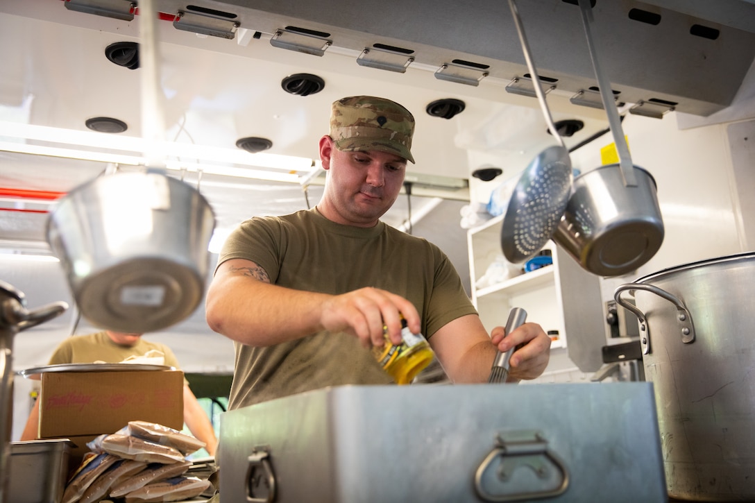 U.S. Army Spc. Chevy Abney of India Company, 429th Brigade Support Battalion, 75th Troop Command, adds ingredients to food in a containerized kitchen during the Regional Philip A. Connelly Field Feeding Competition at the Harlold L. Disney Training Center in Artemus, Kentucky on June 14, 2023. Abney and the rest of India Company are competing against nine other states and territories National Guard field feeding units in the southeast United States for a chance to compete nationally against the other regions of the National Guard. (U.S. Army National Guard photo by Andy Dickson)