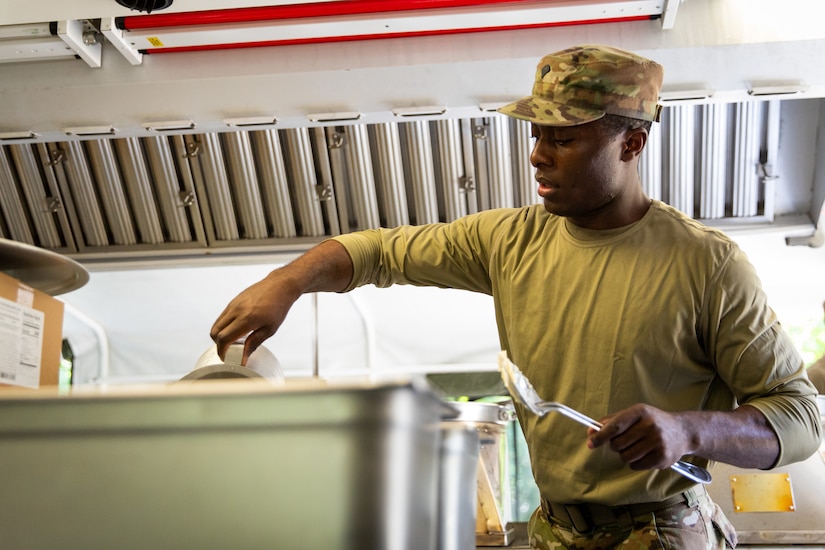 U.S. Army Spc. Adam Bwesi of India Company, 429th Brigade Support Battalion, 75th Troop Command, adds ingredients to a pot in a containerized kitchen during the Regional Philip A. Connelly Field Feeding Competition at the Harlold L. Disney Training Center in Artemus, Kentucky on June 14, 2023. Bwesi and the rest of India Company are competing against nine other states and territories National Guard field feeding units in the southeast United States for a chance to compete nationally against the other regions of the National Guard. (U.S. Army National Guard photo by Andy Dickson)