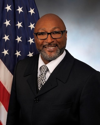Official portrait of a male with an American flag in the background.