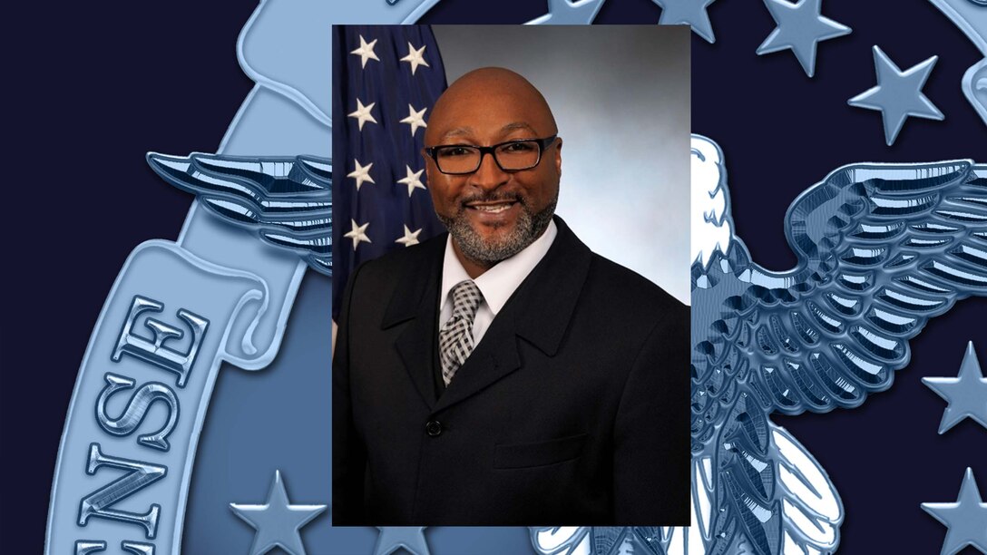 Official portrait of a male with an American flag in the background.