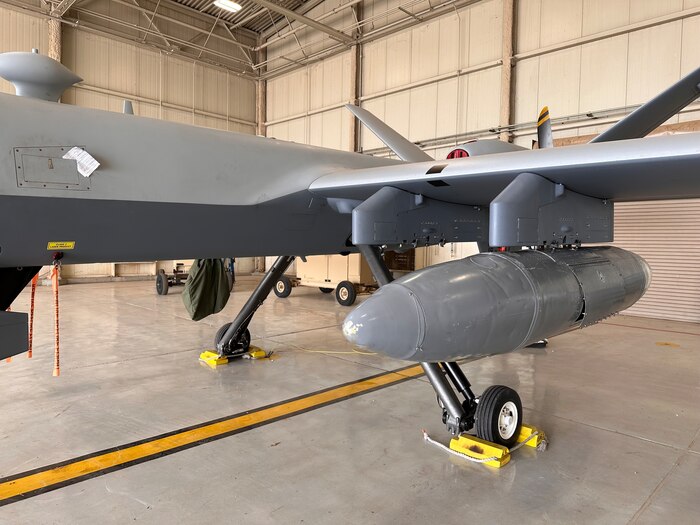 an aircraft sits in a hangar with a resupply capsule attached