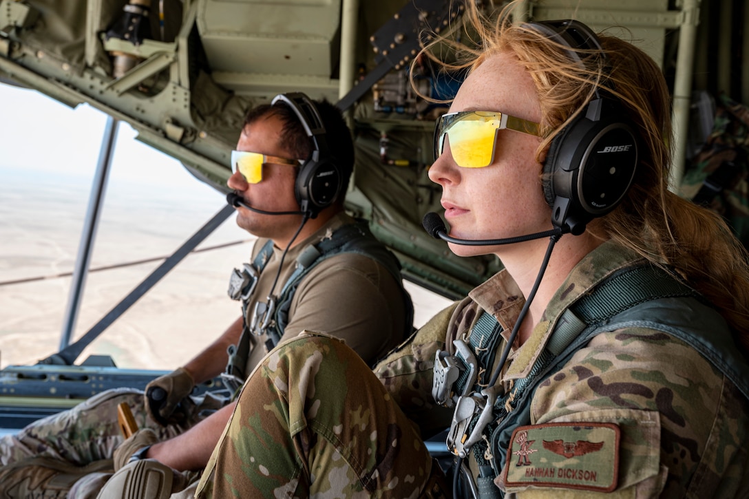 Two airmen wearing sunglasses sit in a cockpit.