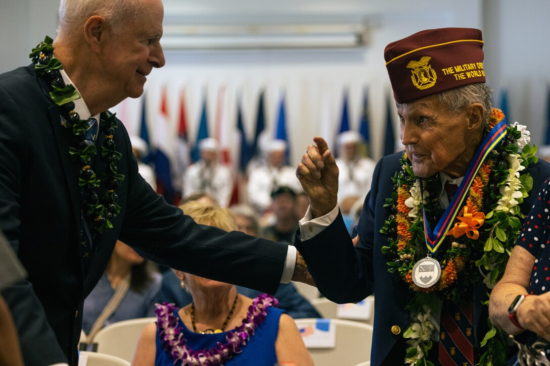 Two Army veterans wearing leis talk during a ceremony.