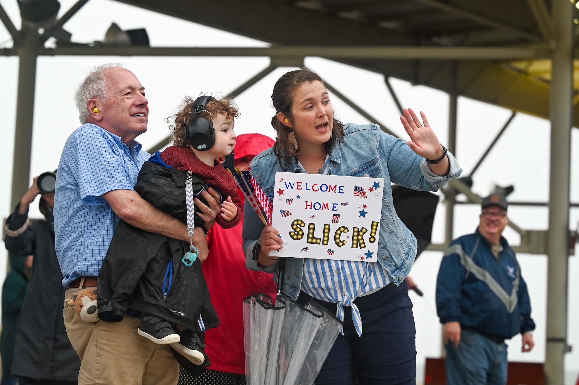 A family waves as redeploying pilots taxi under the sunshades.