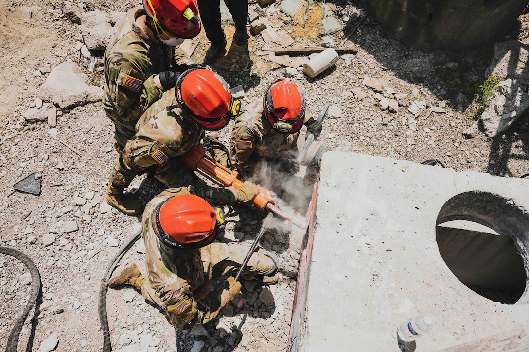 Soldiers use a jackhammer to break through concrete.