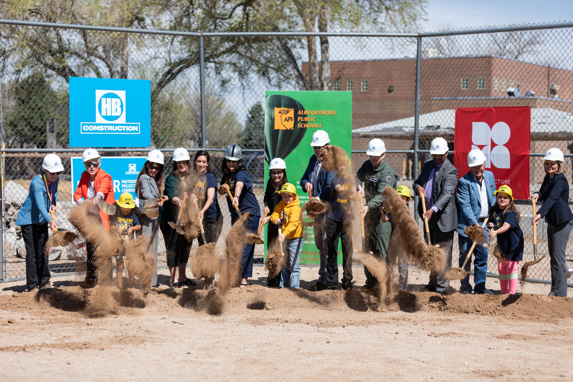 People wearing hardhats, holding shovels, and tossing dirt.