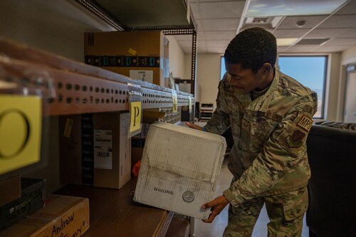 A photo of an Airman grabbing a package from a shelf.