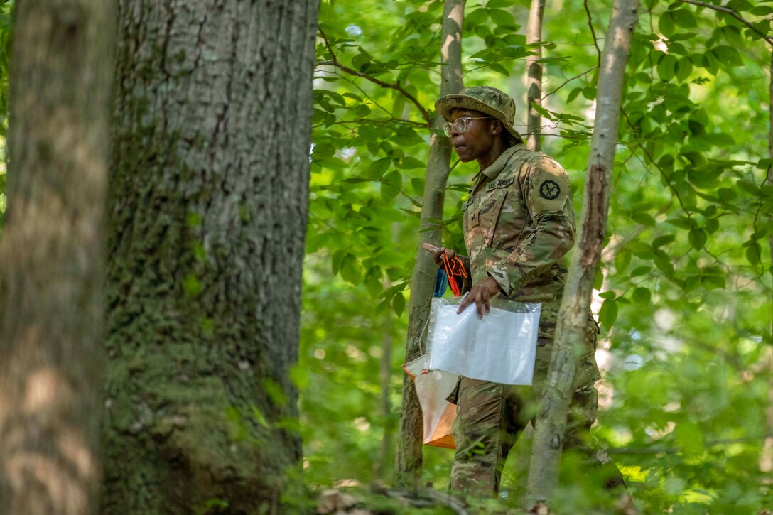 A soldier carrying supplies walks through the woods.