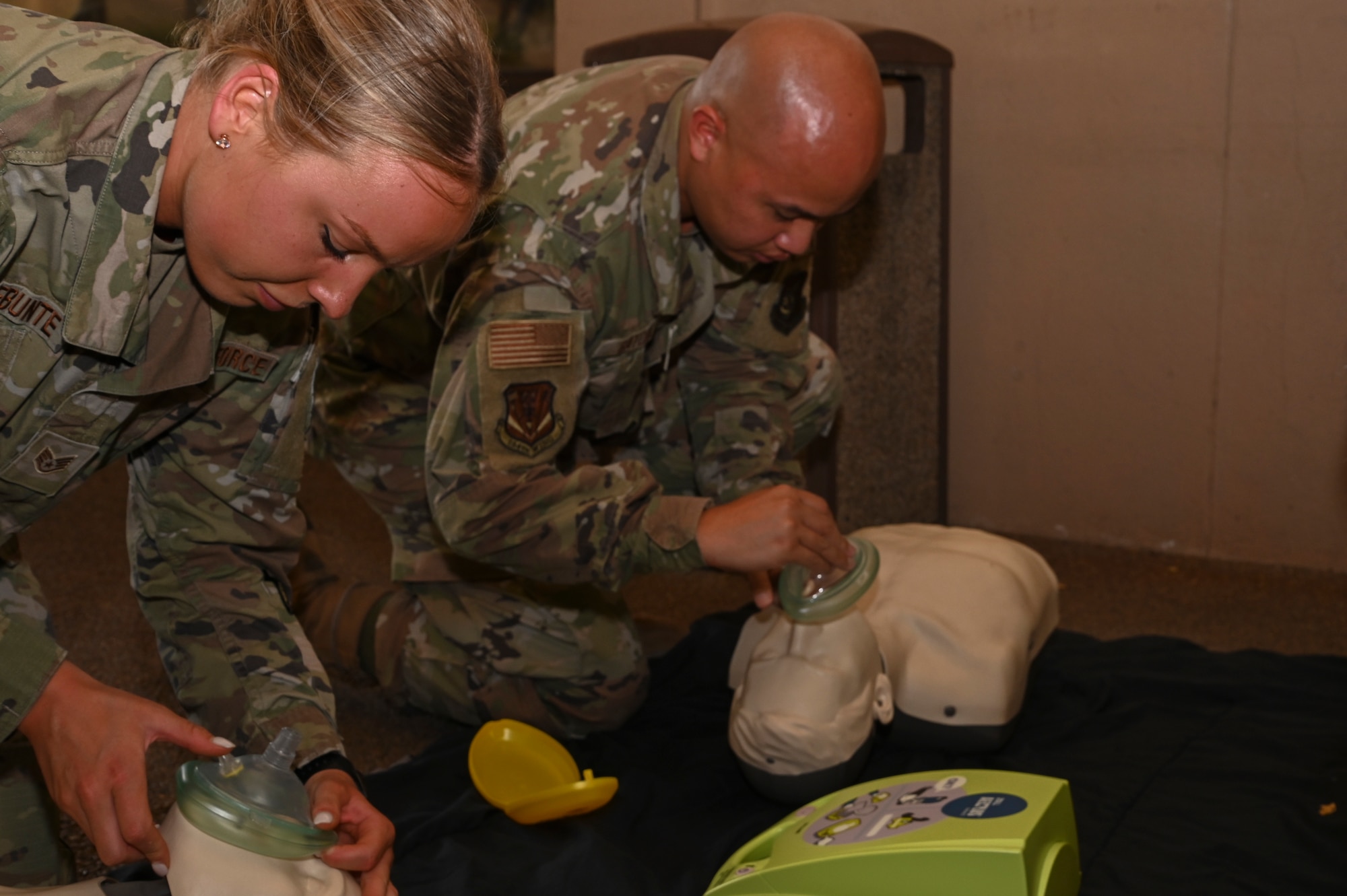 A woman and a man in OCP uniform practice CPR on training mannequins.