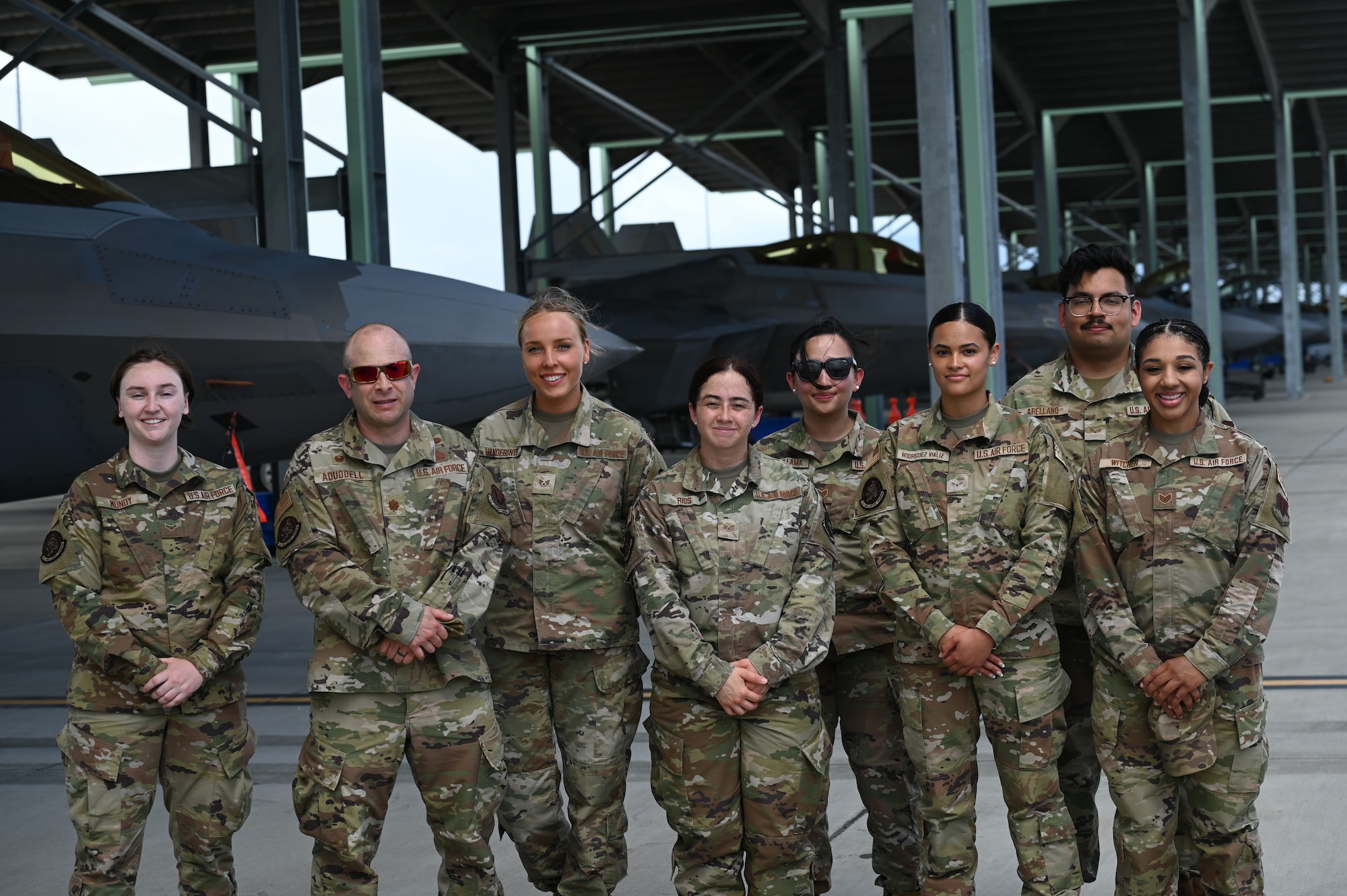 Eight men and women in OCP uniform pose in front of F-22 Raptors.