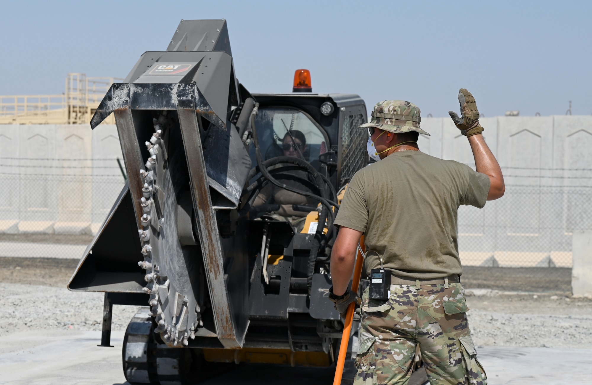 A photo of an Airmen driving a compact track loader with a saw attachment.