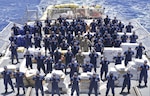 The crew of Coast Guard Cutter Bear (WMEC 901) stands amongst 14,153 pounds of interdicted narcotics at Miami, Florida, June 16, 2023.