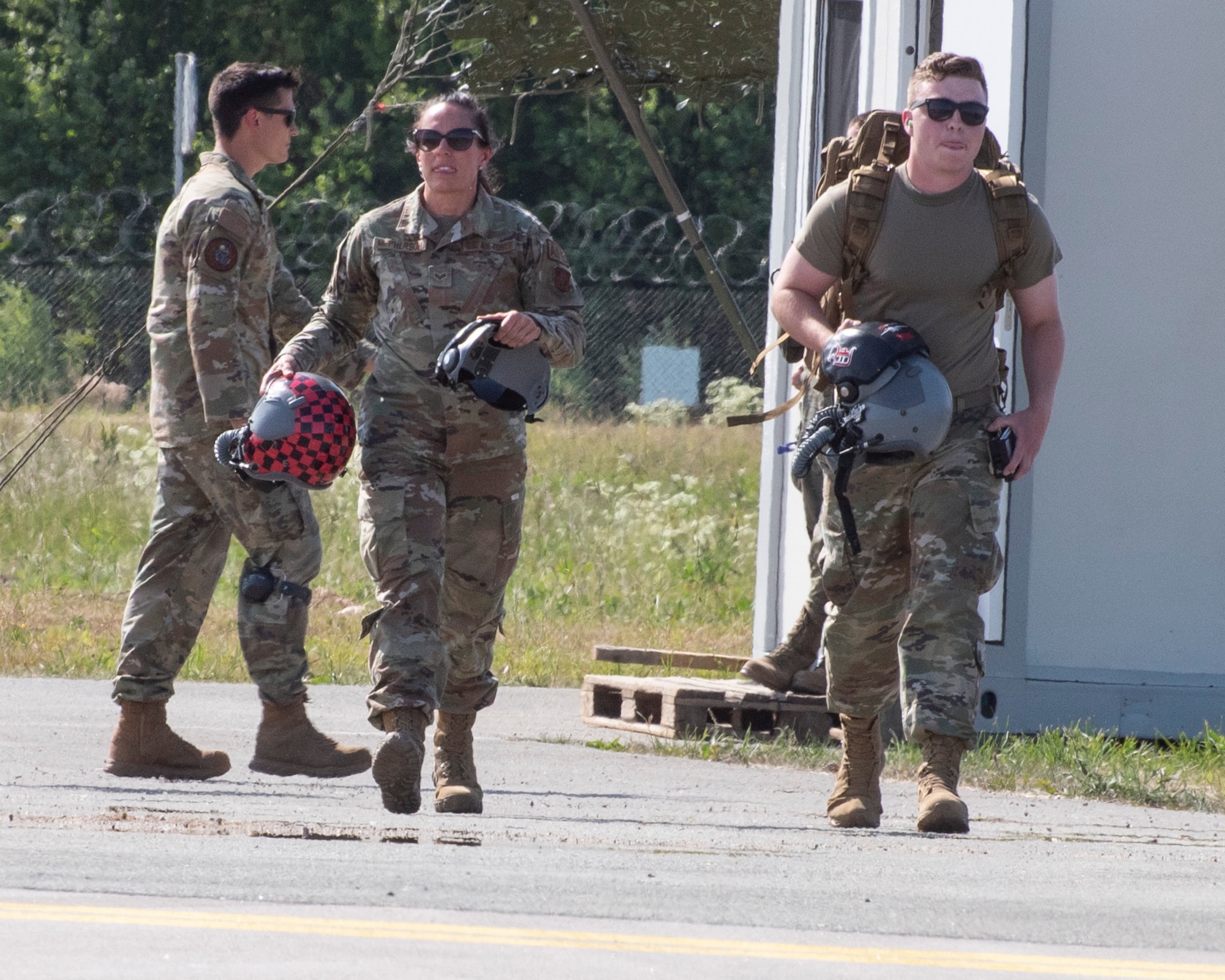 A female Airman (left) and male Airman (right) walk with purpose in forground, carrying pilot helmet and other flight suit gear.
