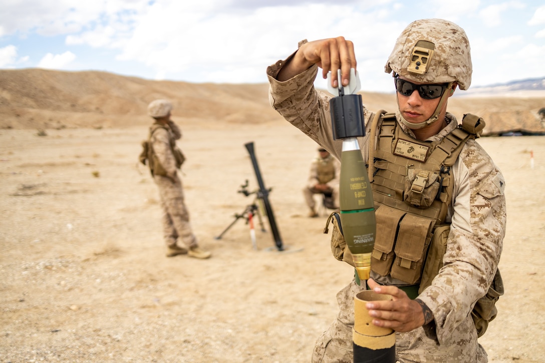 A Marine holds a mortar while another Marine stands behind him.