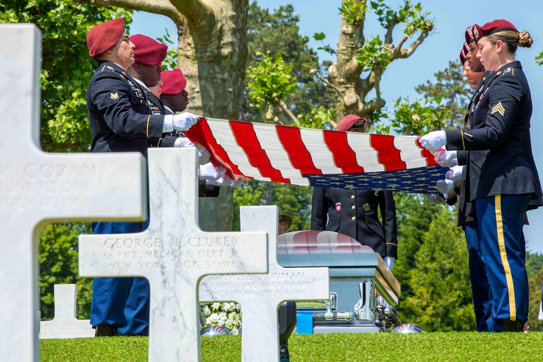 Soldiers hold an American flag over a casket in a cemetery.