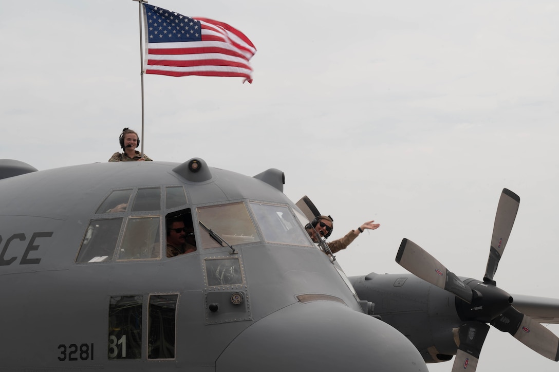 Airmen smile and wave from a military aircraft.